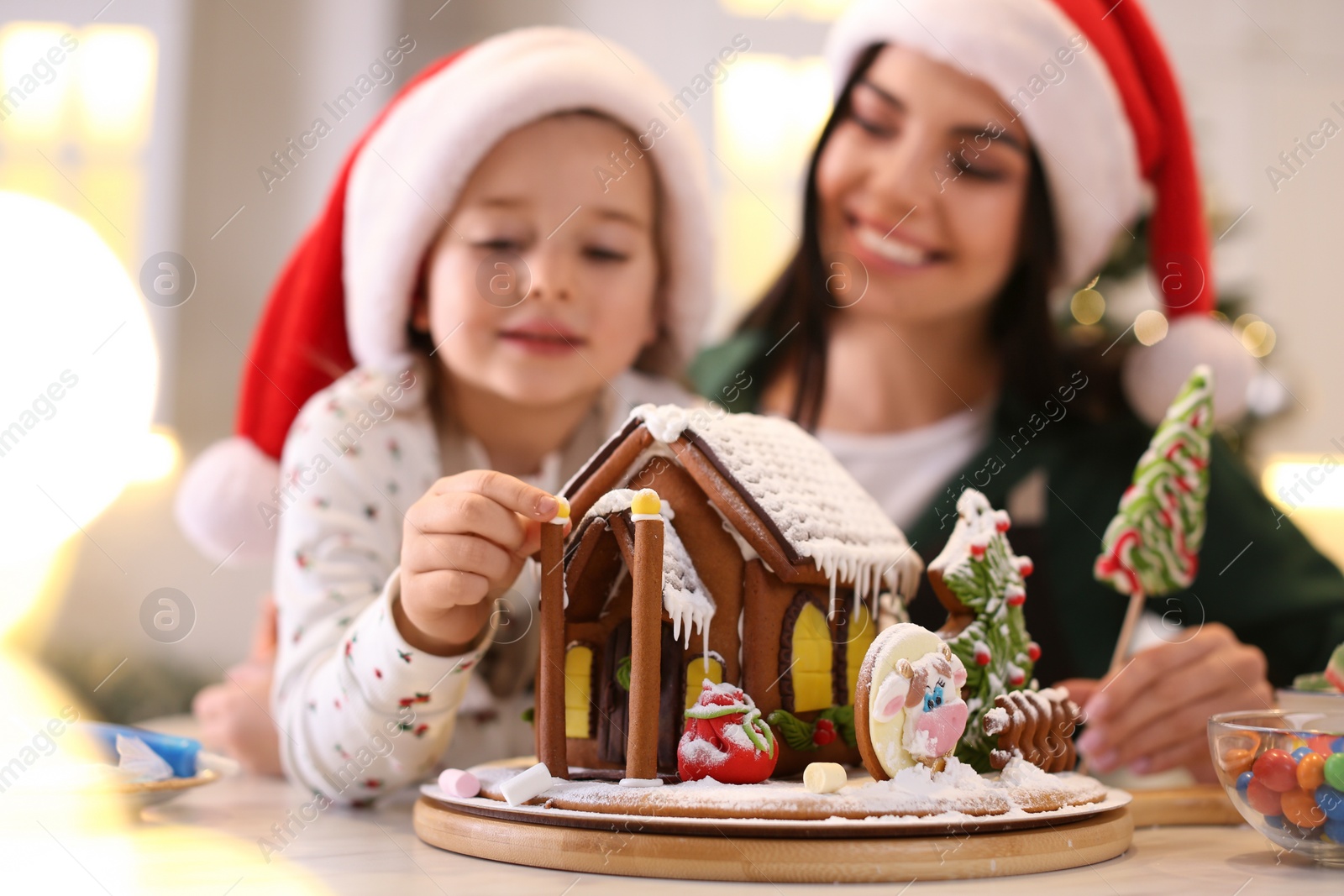 Photo of Mother and daughter decorating gingerbread house at table indoors