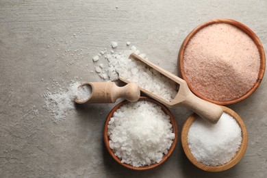 Photo of Different natural salt on grey textured table, flat lay. Space for text