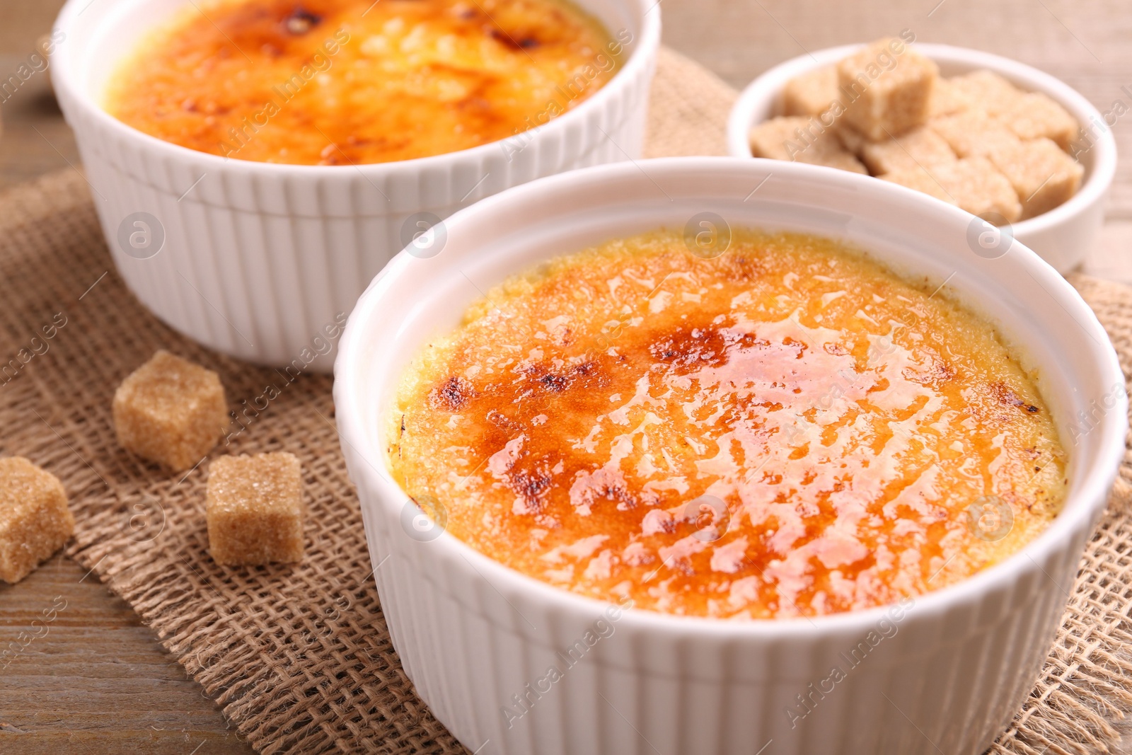 Photo of Delicious creme brulee in bowls and sugar cubes on wooden table, closeup