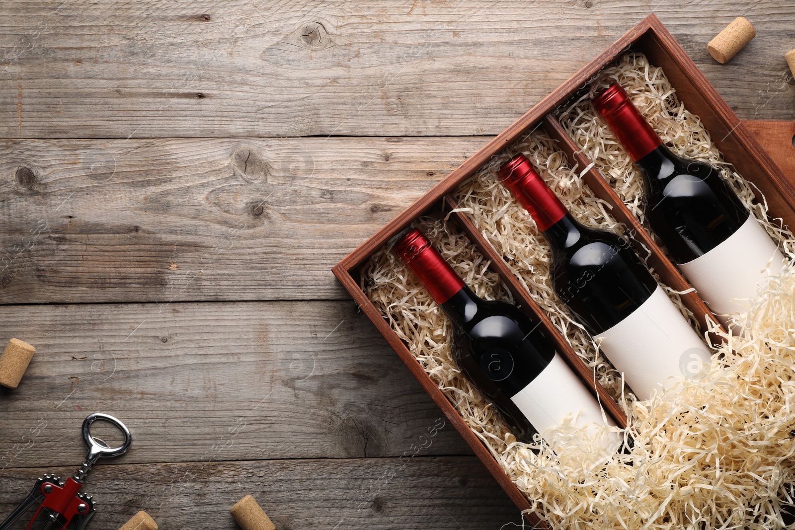 Photo of Box with wine bottles, corkscrew and corks on wooden table, flat lay. Space for text