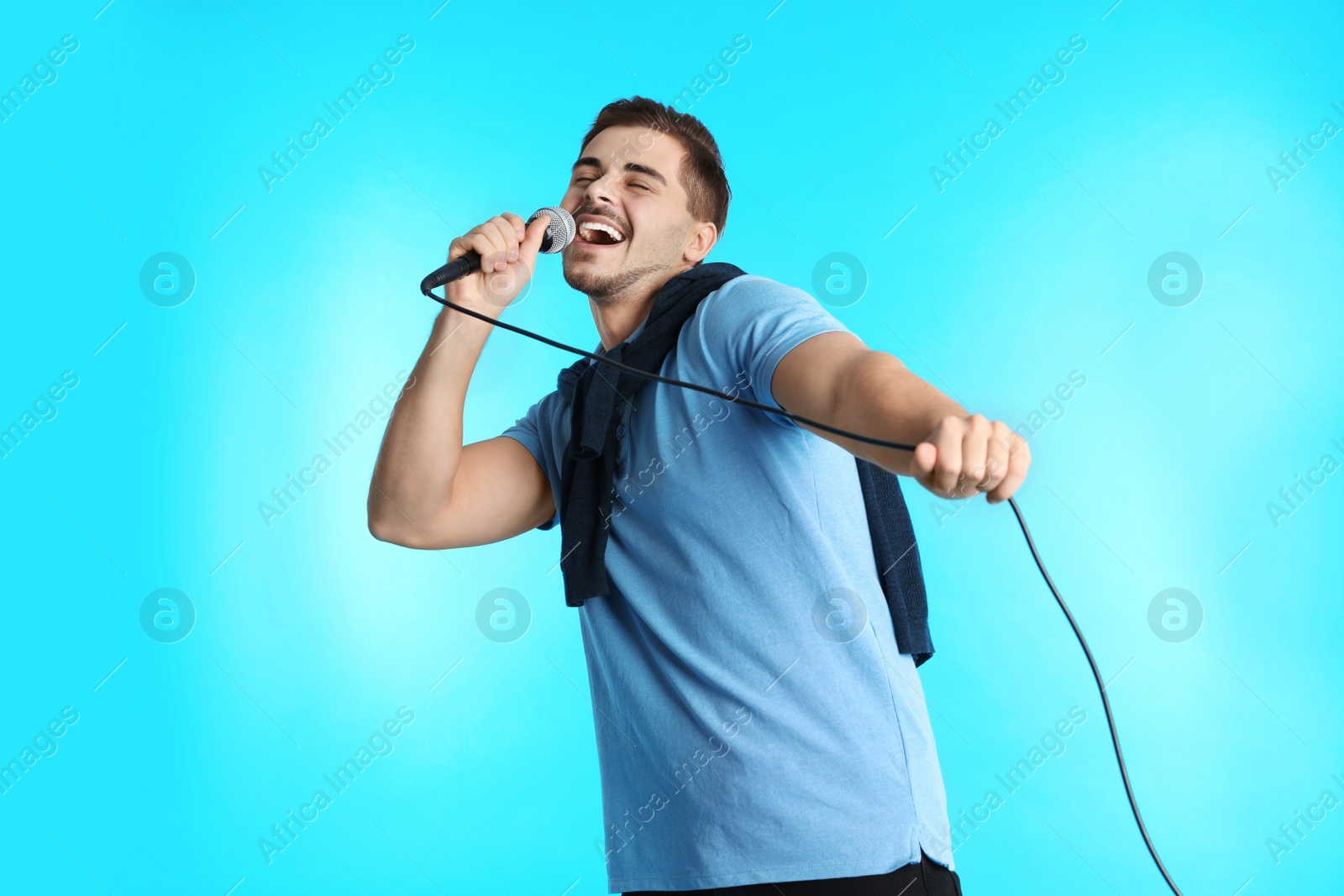 Photo of Young handsome man in casual clothes singing with microphone on color background