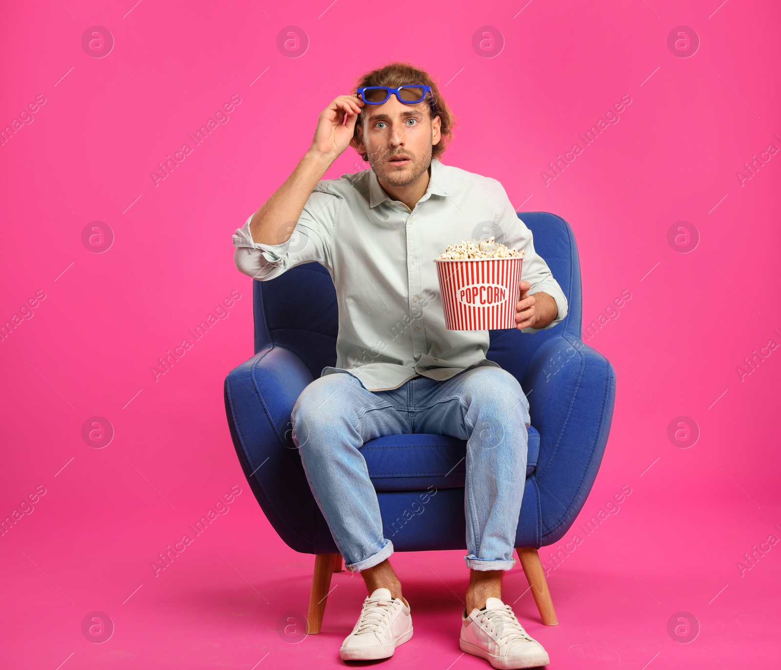 Photo of Emotional man with 3D glasses and popcorn sitting in armchair during cinema show on color background