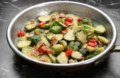 Photo of Delicious cooked Brussels sprouts with bacon in pan on marble table, closeup