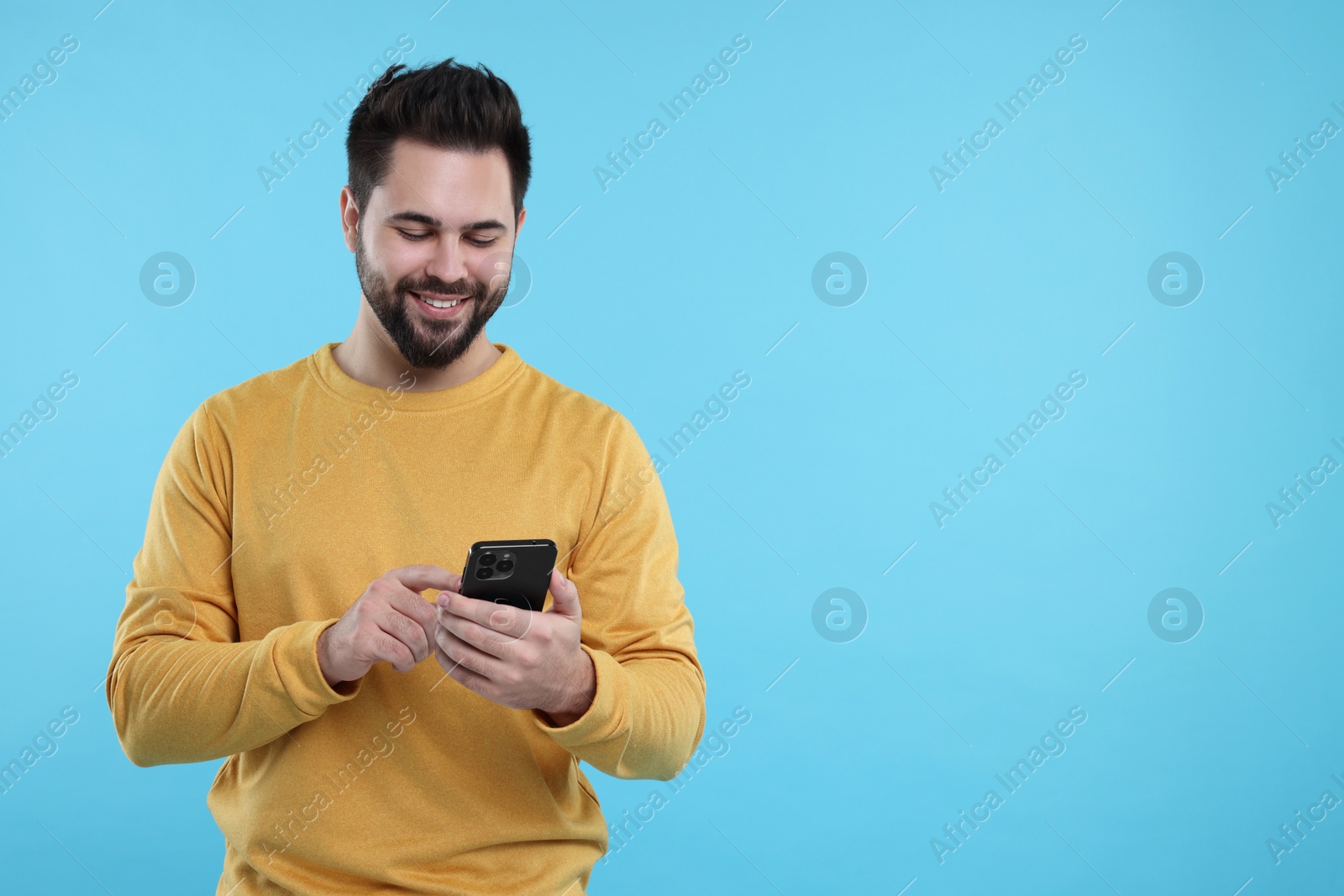 Photo of Happy young man using smartphone on light blue background, space for text