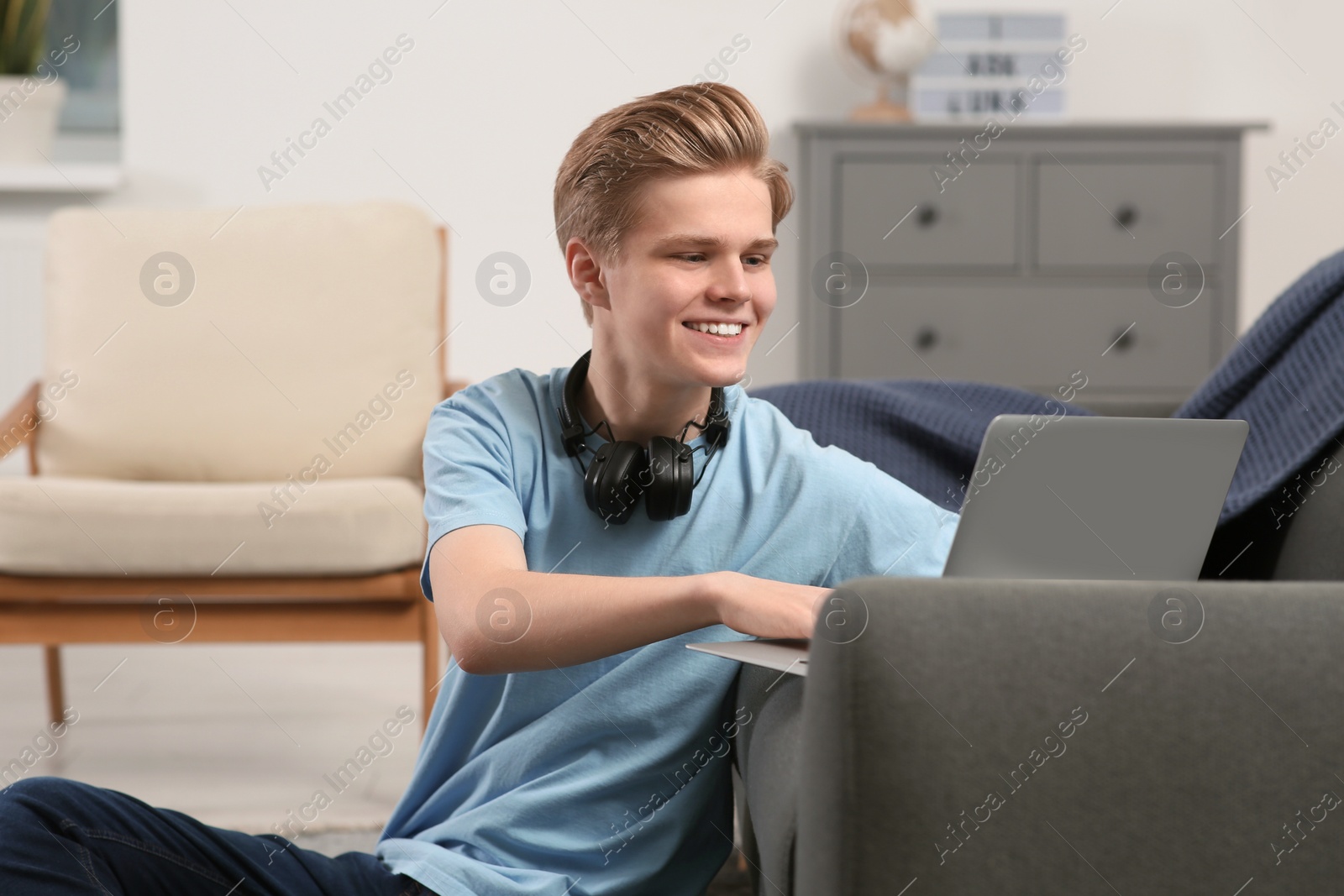 Photo of Online learning. Smiling teenage boy typing on laptop at home