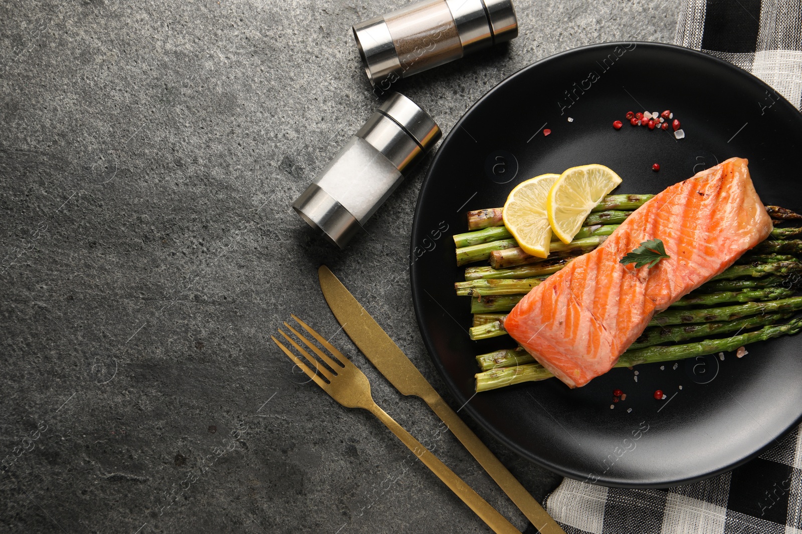 Photo of Tasty grilled salmon with asparagus, lemon and spices served on gray table, flat lay. Space for text