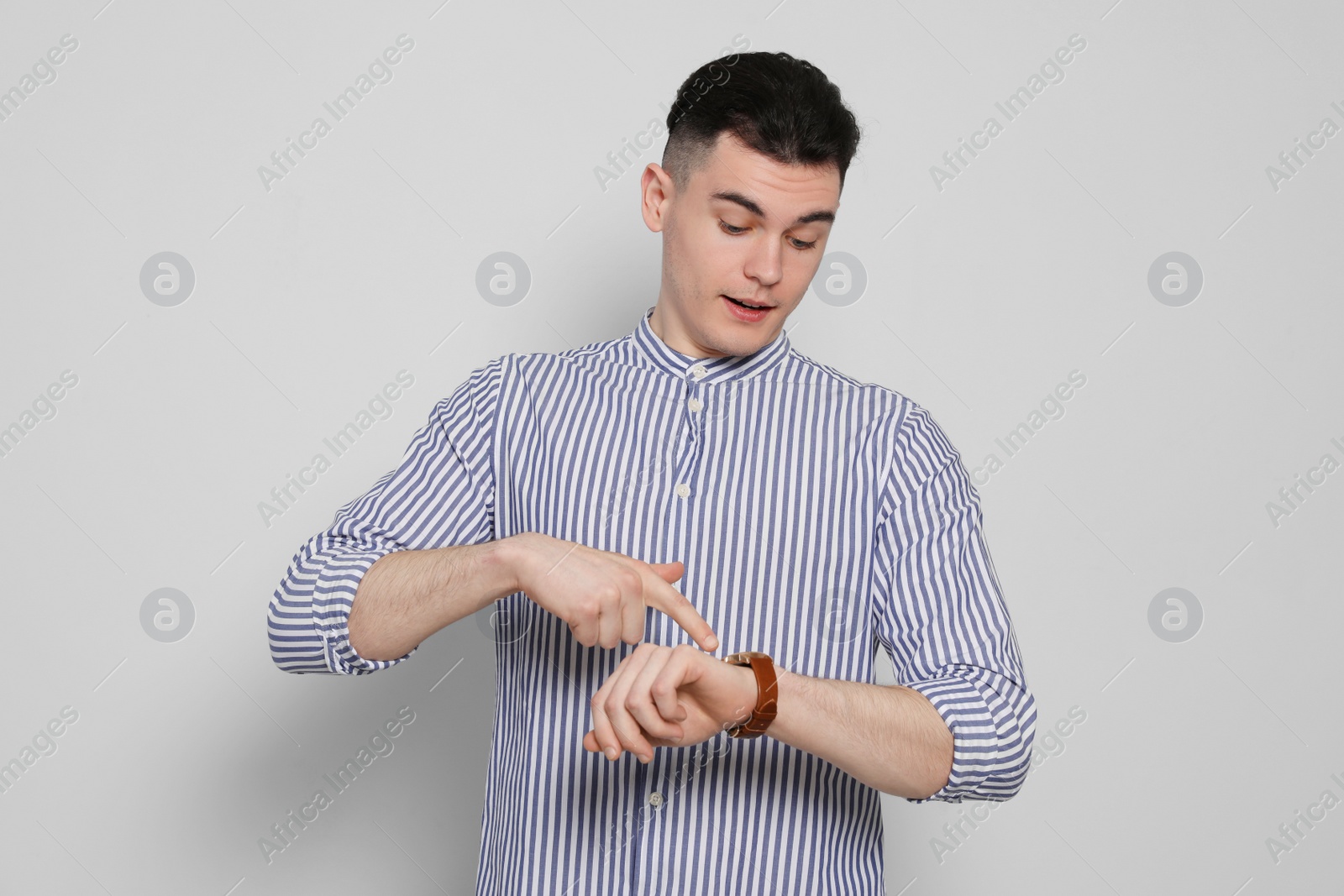 Photo of Emotional young man checking time on light grey background. Being late concept