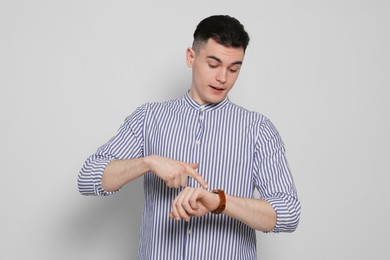 Emotional young man checking time on light grey background. Being late concept