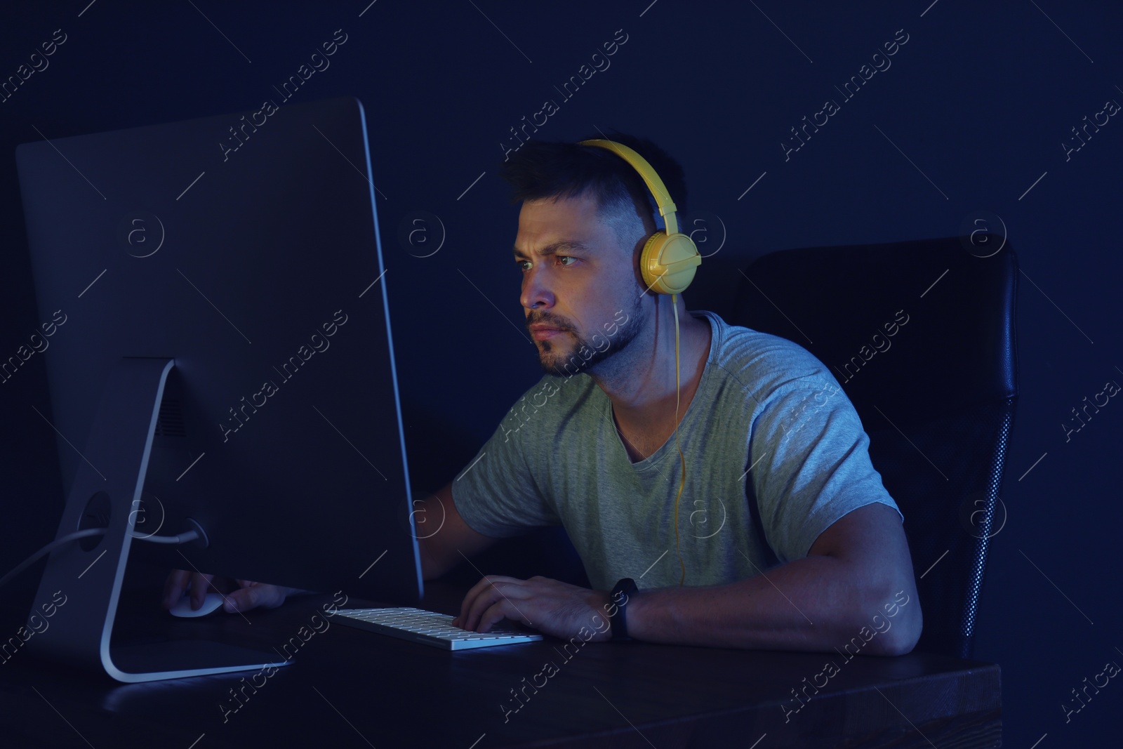 Photo of Man with headphones playing video game on modern computer in dark room