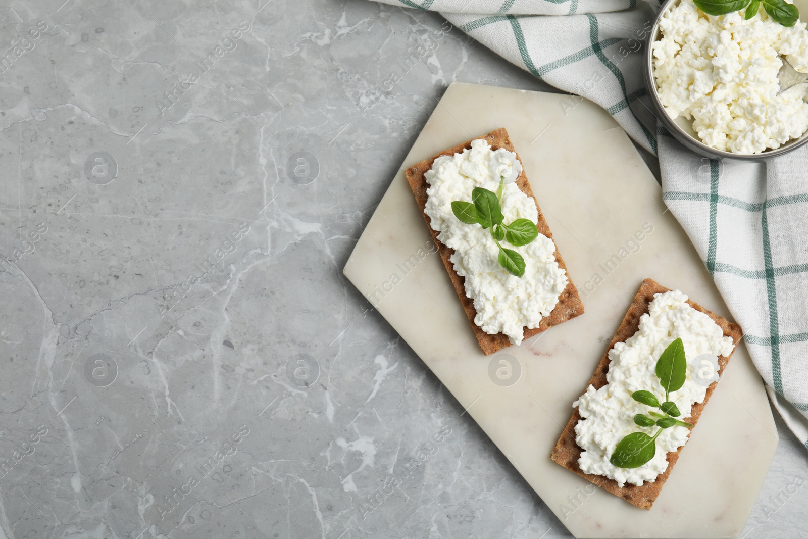 Photo of Crispy crackers with cottage cheese and basil on light grey marble table, flat lay. Space for text