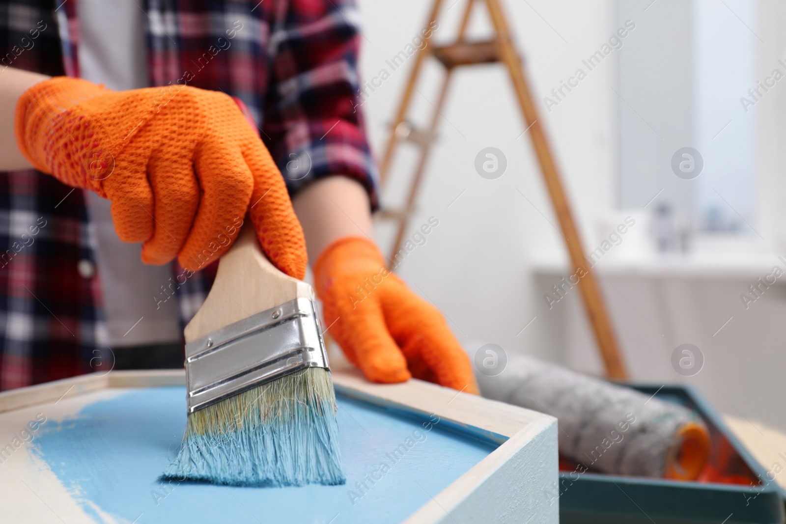 Photo of Woman painting honeycomb shaped shelf with brush indoors, closeup. Space for text