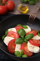 Photo of Caprese salad with tomatoes, mozzarella, basil and spices in bowl, closeup