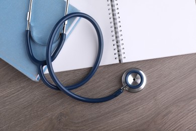 Book, stethoscope and notebook on wooden table, flat lay. Medical education