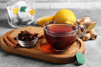 Photo of Tea bags, cuphot drink, cookies and ingredients on light grey table