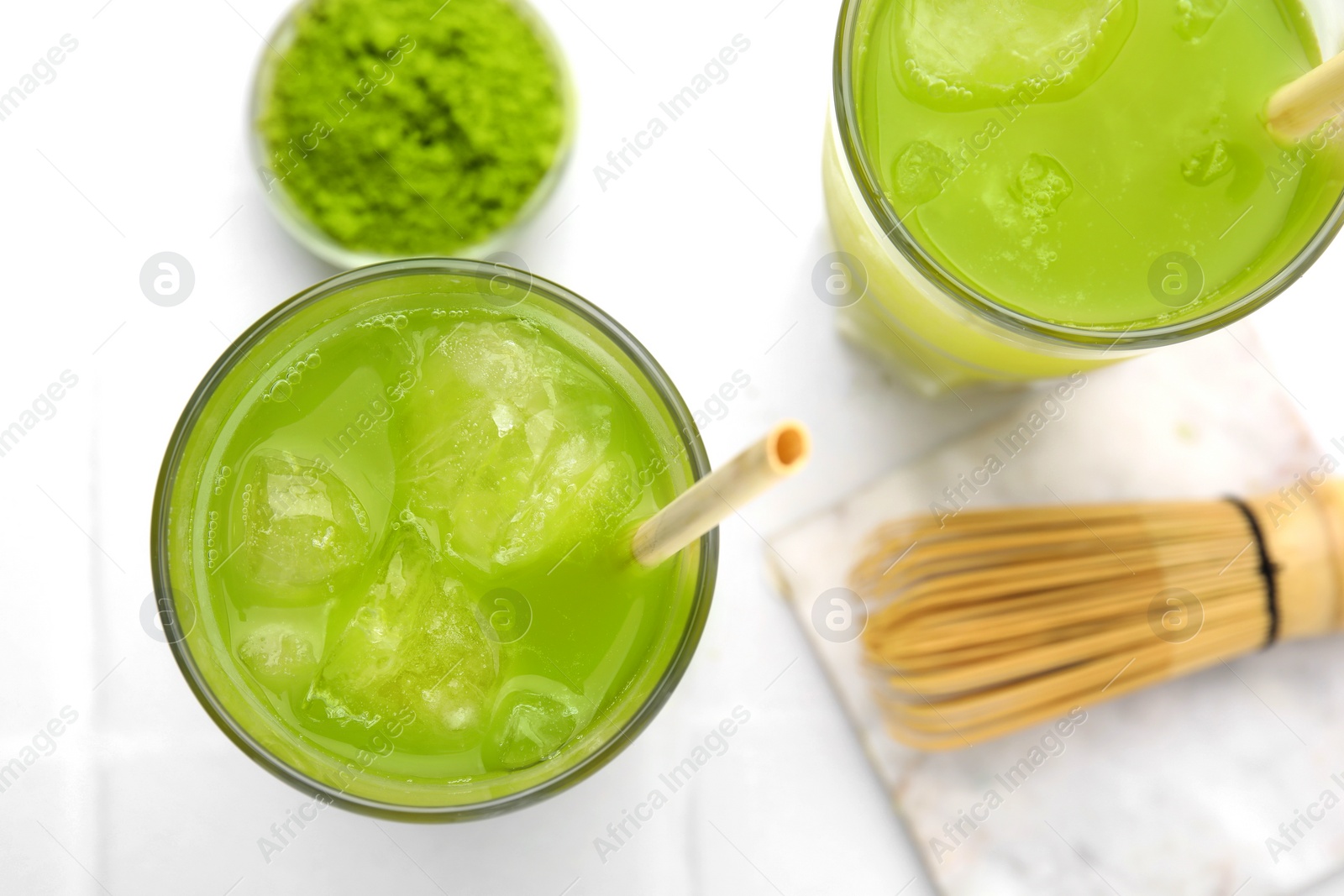 Photo of Delicious iced green matcha tea, powder and bamboo whisk on white table, flat lay