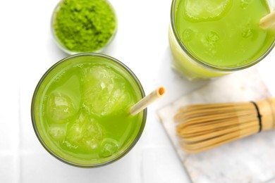 Delicious iced green matcha tea, powder and bamboo whisk on white table, flat lay