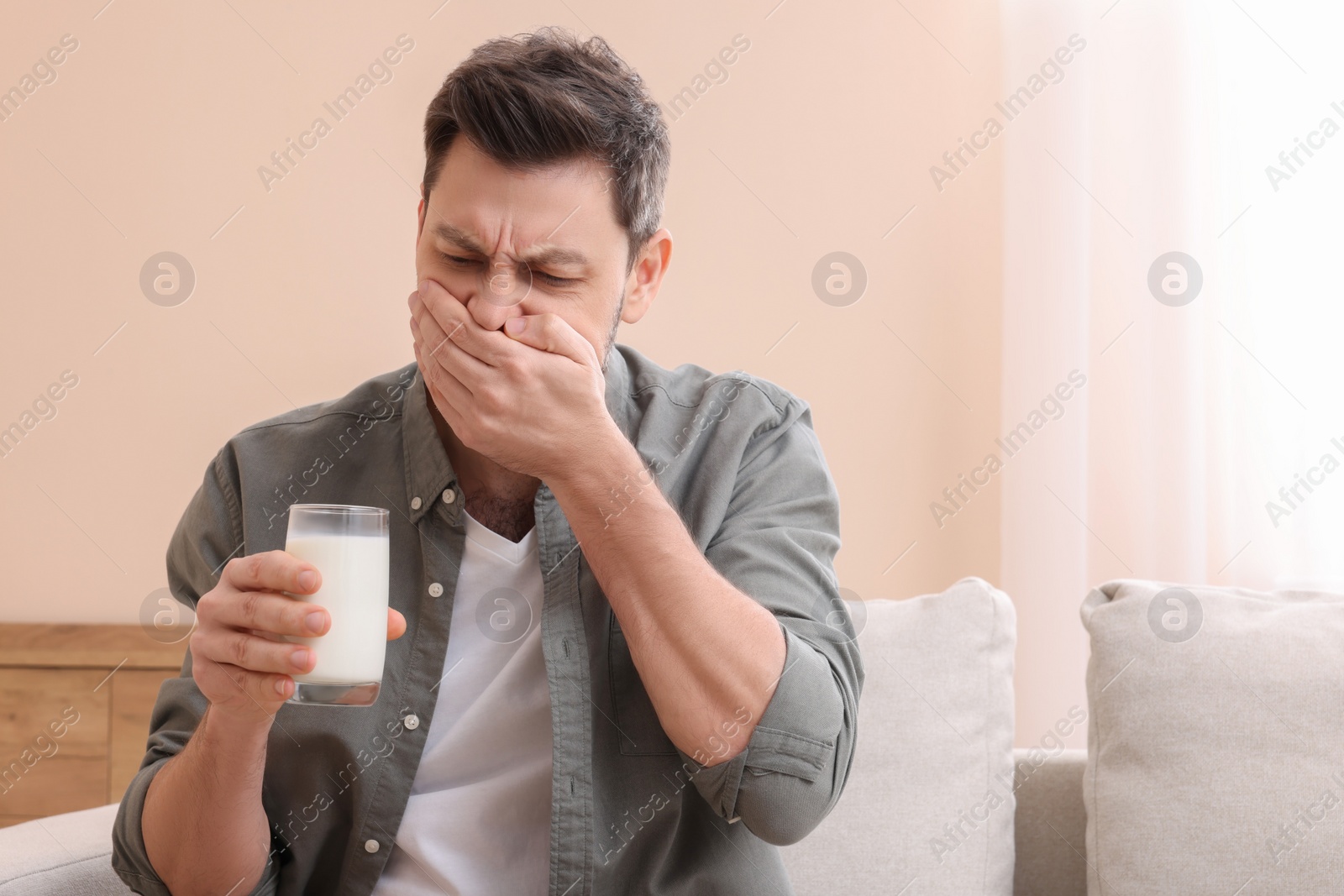 Photo of Man with glass of milk suffering from lactose intolerance at home, space for text