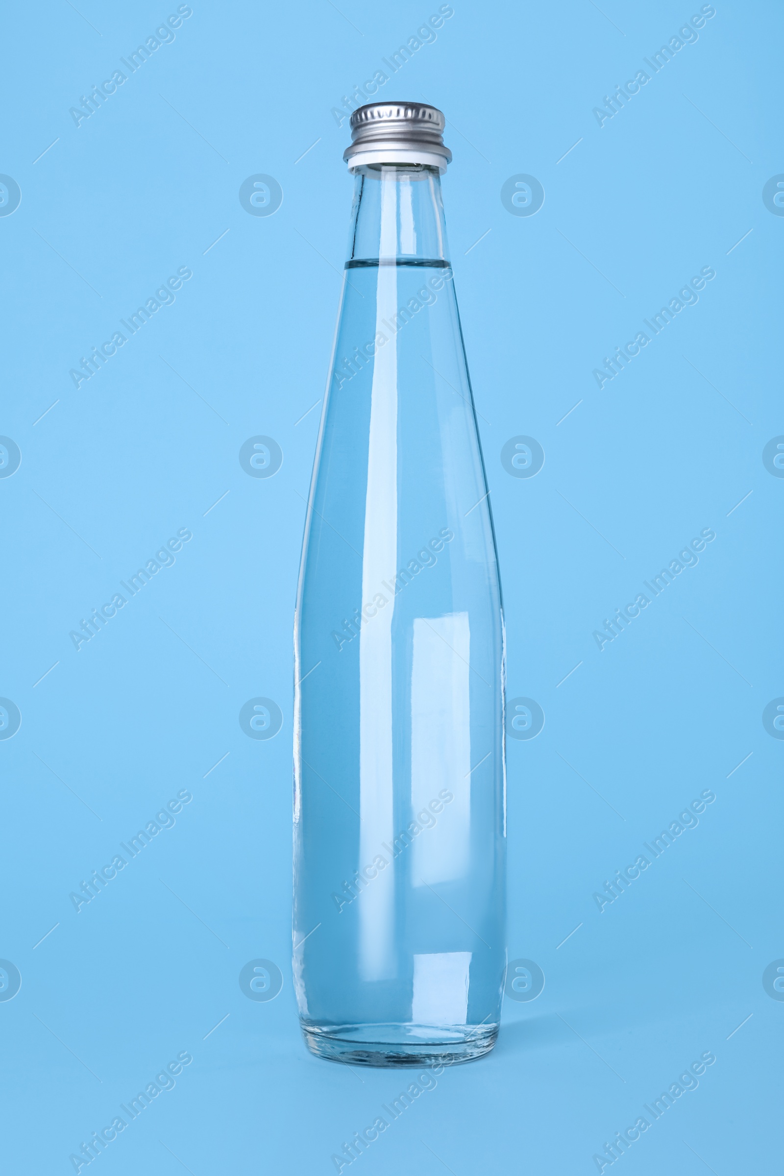 Photo of Glass bottle with water on light blue background