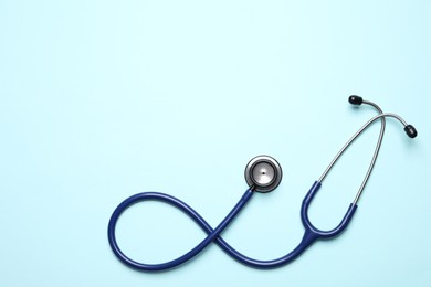 Stethoscope on light blue background, top view. Space for text