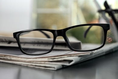 Photo of Stack of newspapers and glasses on grey table indoors, closeup