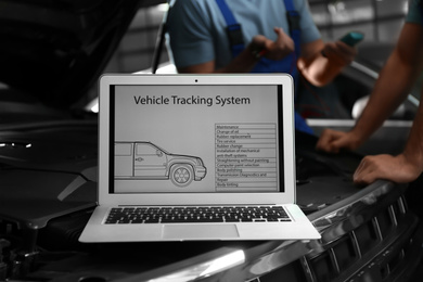 Photo of Laptop with vehicle tracking system and blurred mechanics on background. Auto diagnostic
