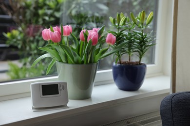 Beautiful bouquet with pink tulips, potted lily and modern thermostat on white window sill indoors