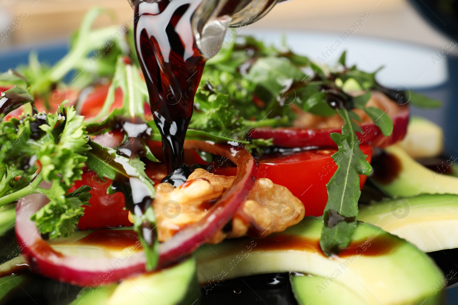 Photo of Pouring balsamic vinegar onto vegetable salad, closeup