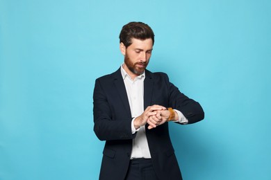 Handsome bearded man looking at wristwatch on light blue background