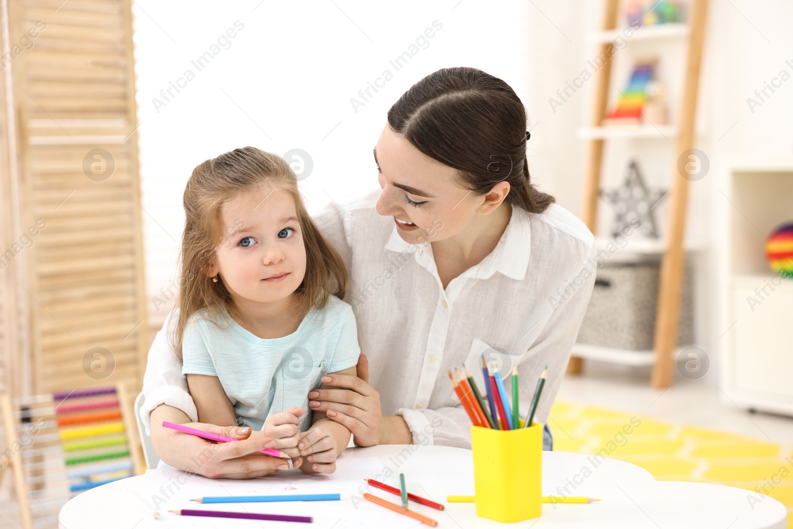 Photo of Mother and her little daughter drawing with colorful pencils at home