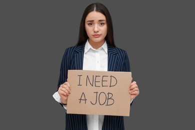 Photo of Young unemployed woman holding sign with phrase I Need A Job on black background