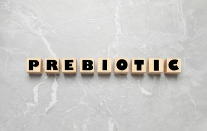 Wooden cubes with word Prebiotic on light grey marble table, flat lay