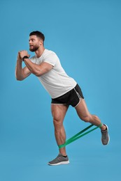 Photo of Young man exercising with elastic resistance band on light blue background