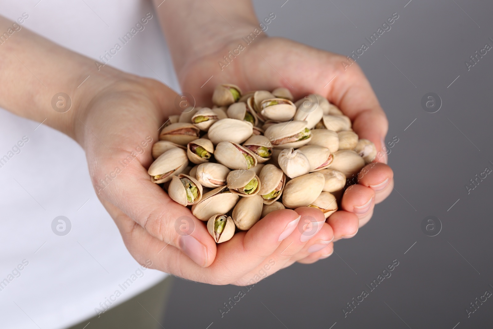 Photo of Woman holding handful of tasty pistachios on grey background, closeup