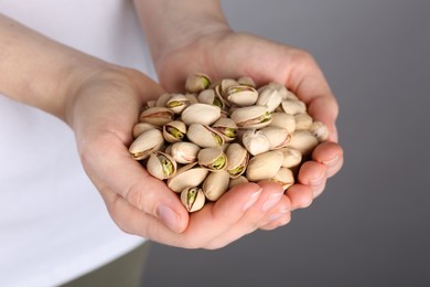 Woman holding handful of tasty pistachios on grey background, closeup