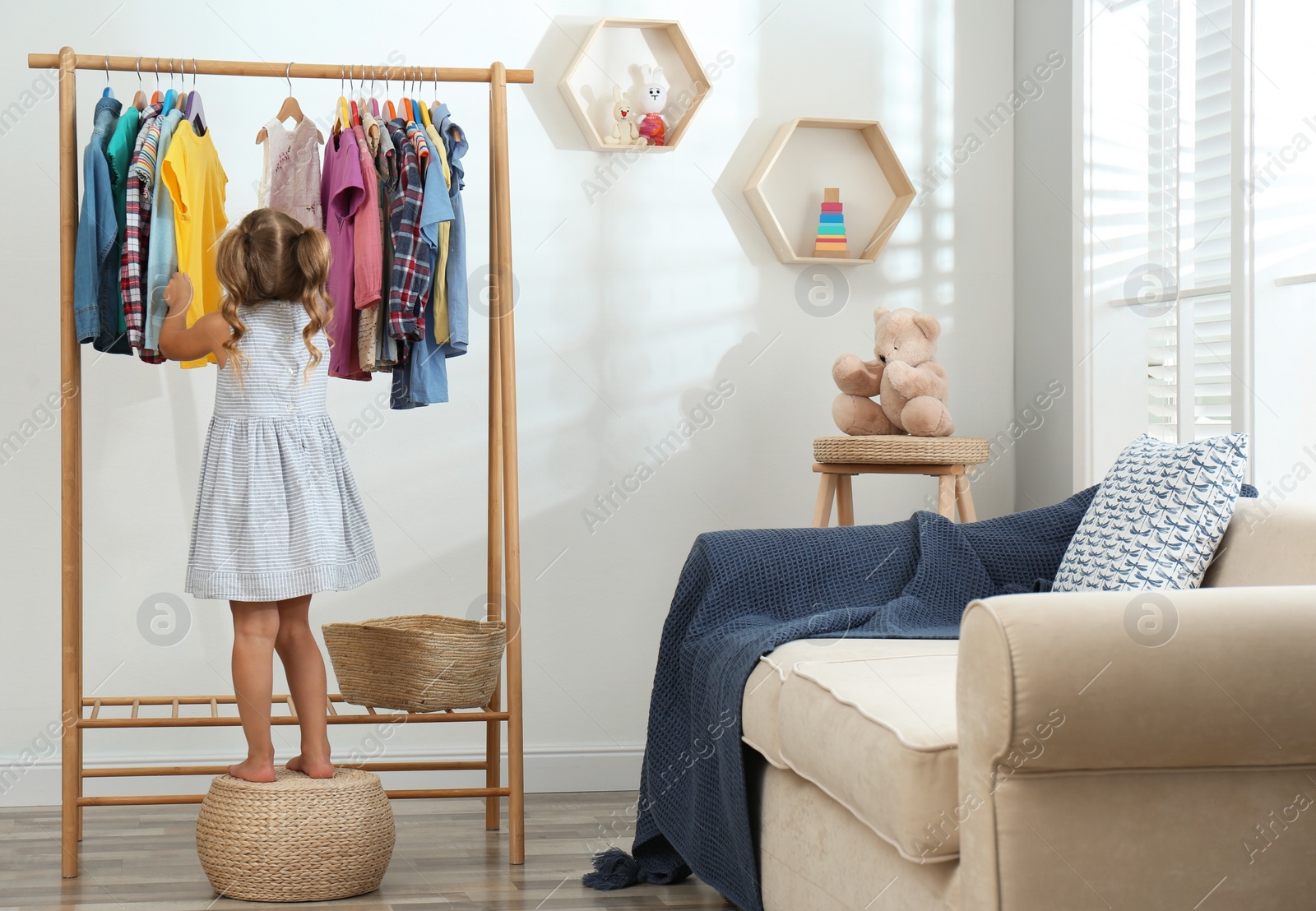 Photo of Little girl choosing clothes on rack in living room