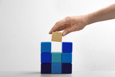 Photo of Woman putting wooden block to colorful cubes on white background, closeup. Career promotion concept