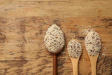Photo of Spoons with raw quinoa seeds on wooden table, flat lay. Space for text