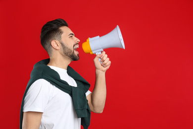 Young man with megaphone on red background. Space for text