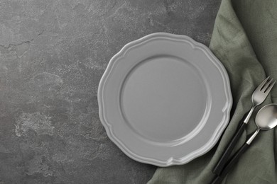 Stylish setting with cutlery, napkin and plate on grey textured table, top view. Space for text