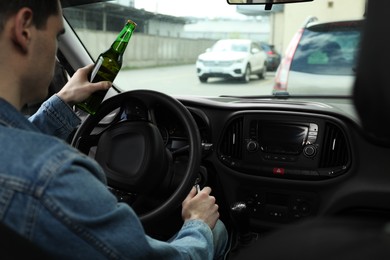 Man with bottle of beer driving car, closeup. Don't drink and drive concept