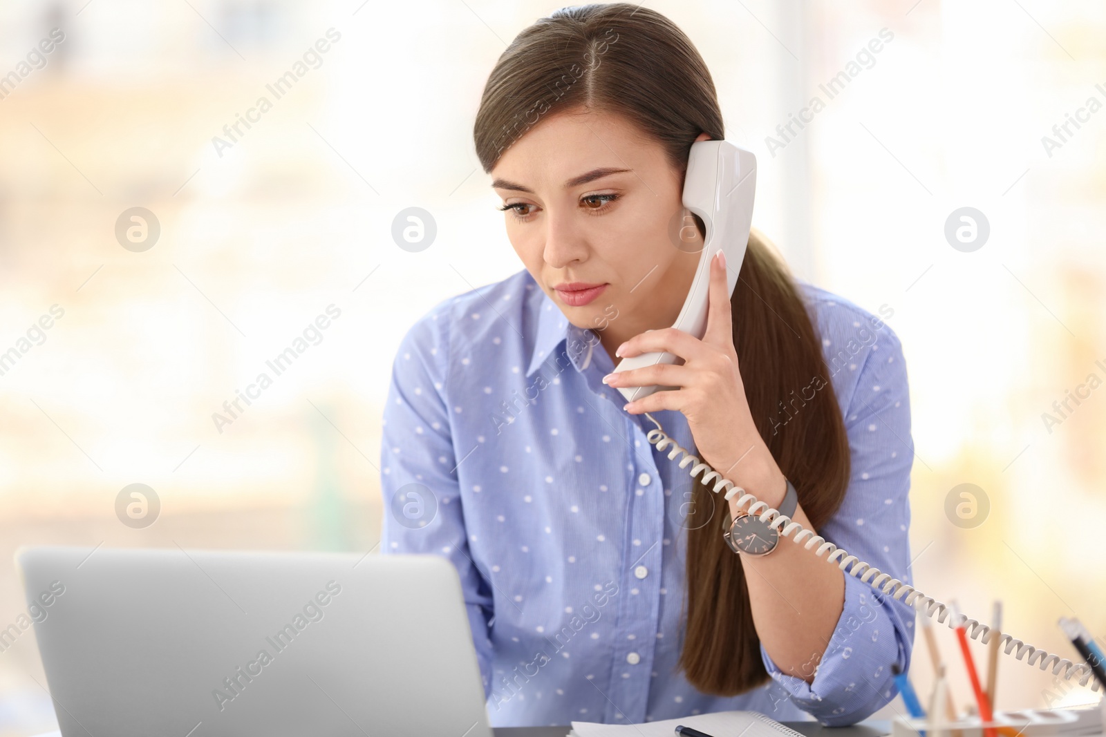 Photo of Young woman talking on phone at workplace