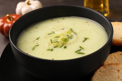 Photo of Bowl of tasty leek soup and bread on table, closeup