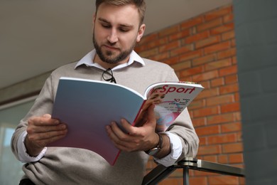 Photo of Young business man reading sports magazine indoors
