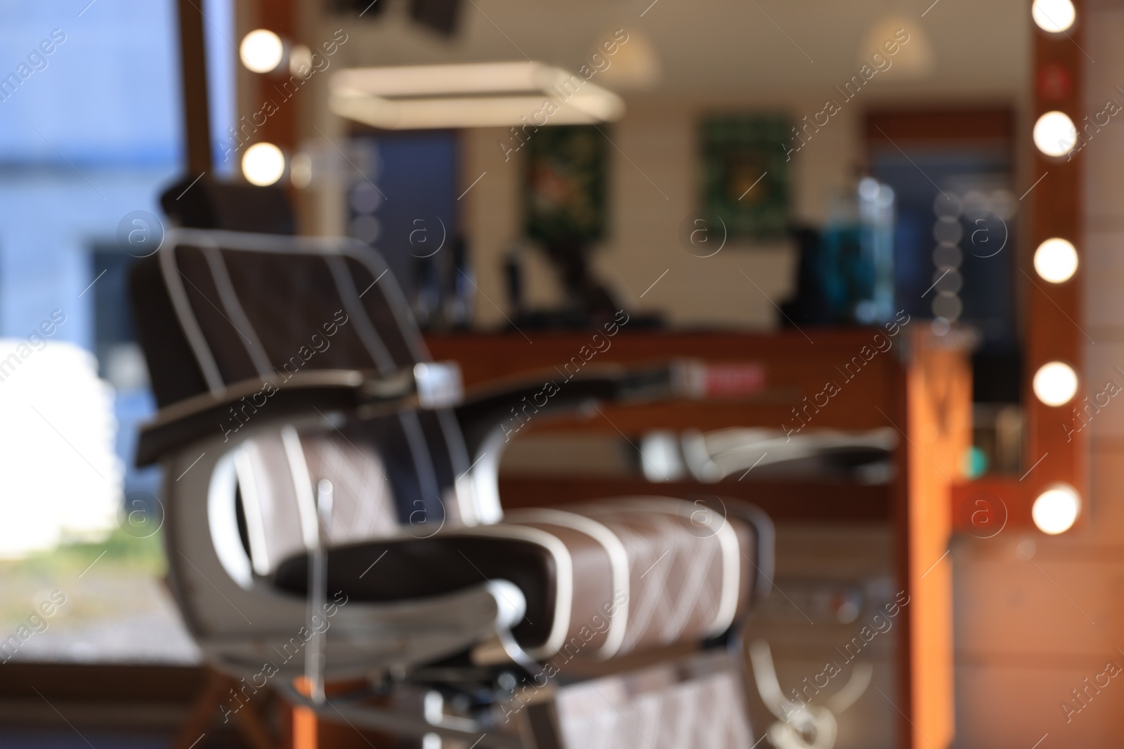 Photo of Blurred view of stylish hairdresser's workplace with professional armchair in barbershop