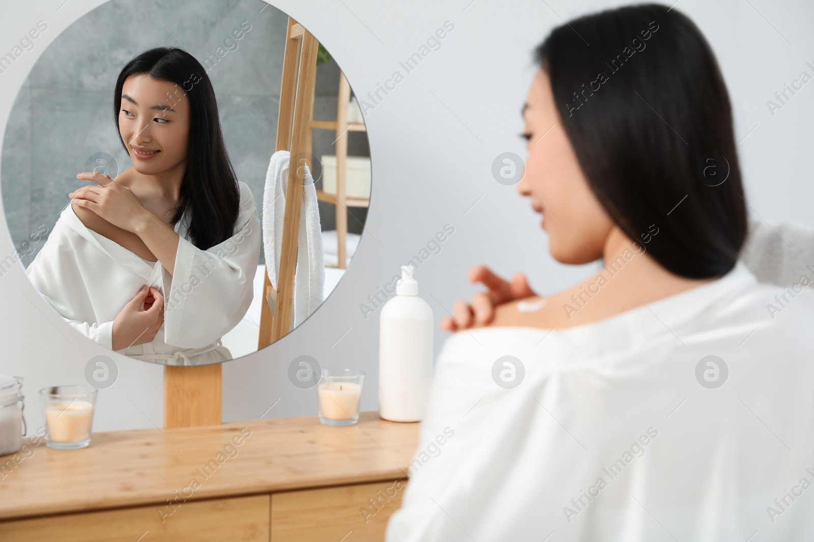 Photo of Beautiful young Asian woman applying body cream on shoulder in bathroom