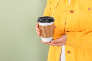 Woman holding takeaway cup with drink on pale green background, closeup view and space for text. Coffee to go