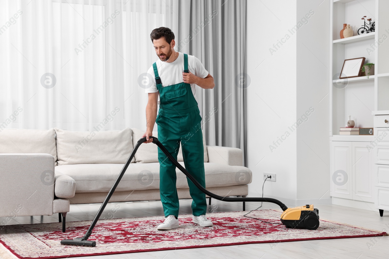 Photo of Dry cleaner's employee hoovering carpet with vacuum cleaner in room