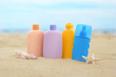 Different bottles with sun protection creams and seashells on sandy beach near sea