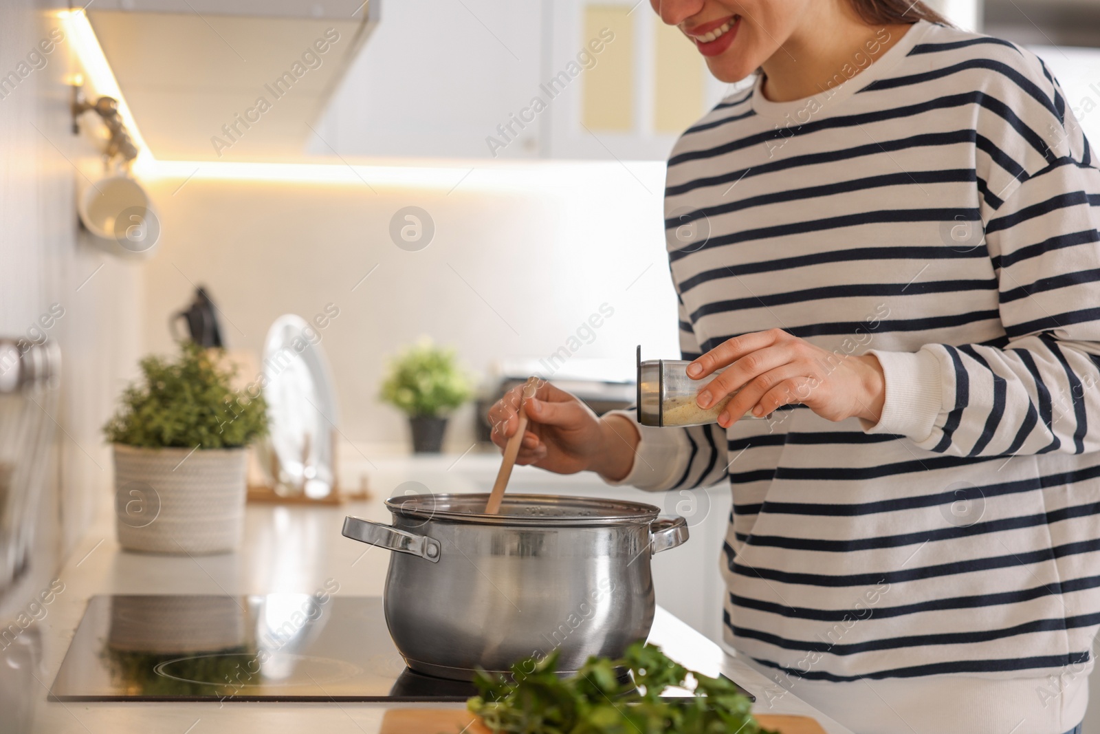 Photo of Smiling woman adding spices into pot with soup in kitchen, closeup