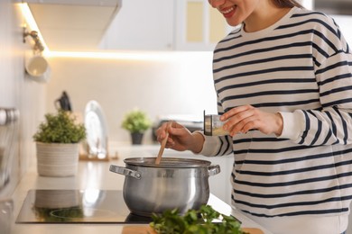 Smiling woman adding spices into pot with soup in kitchen, closeup